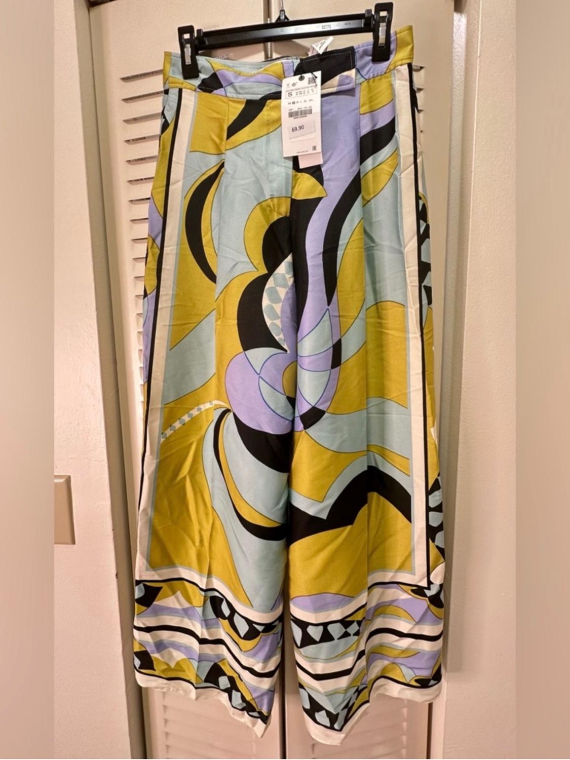 Printed trousers in shades of yellow, lilac, and black hanging on a hanger. Visible tag with price of 69.90.