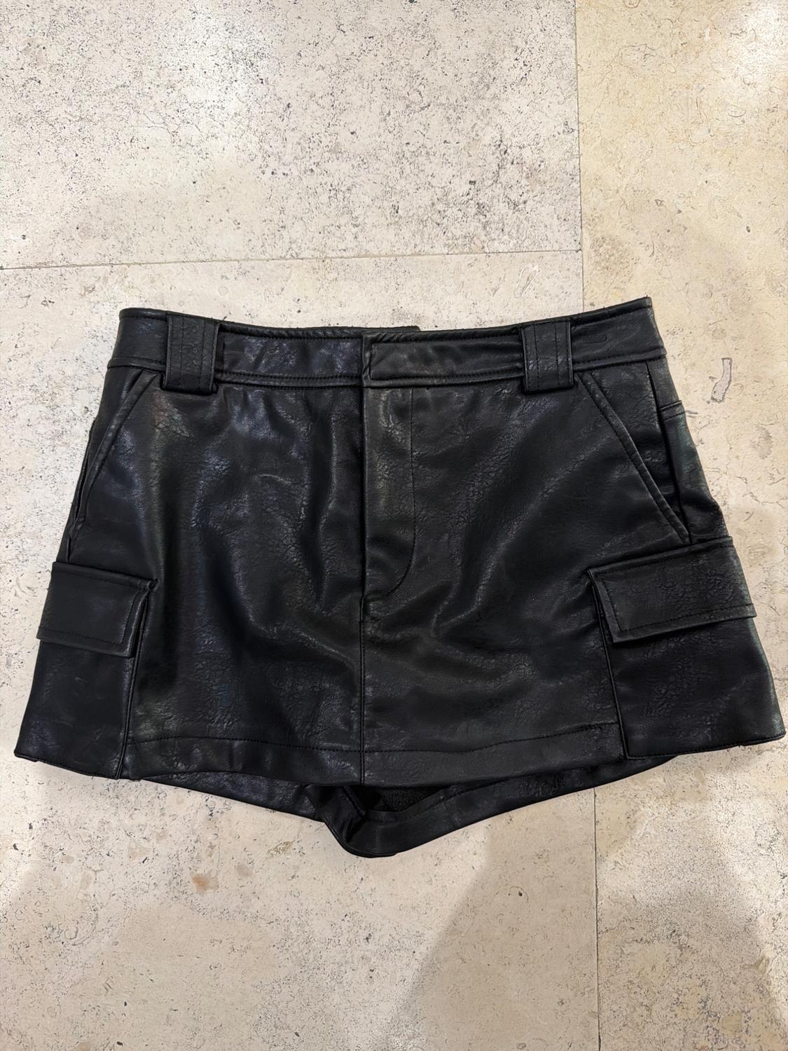 Black faux-leather skort with cargo pockets, laid out on a light stone-tiled floor with a relaxed aesthetic.