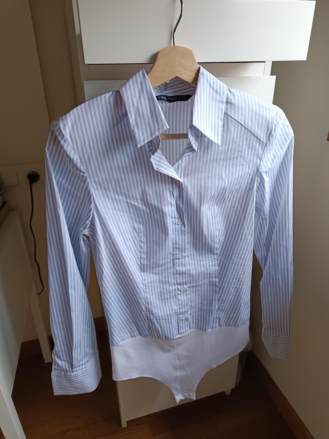 Blue and white striped shirt hanging on a wooden hanger, with a background of white furniture and a wooden floor.