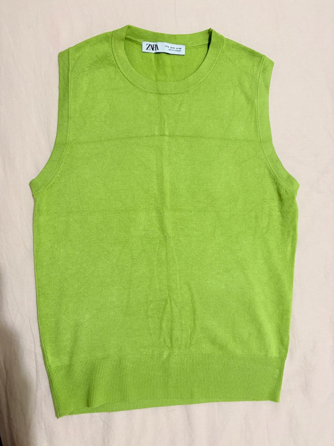 Bright green sleeveless round-neck knit top against a light-coloured fabric background. Neck label with the text ZARA.