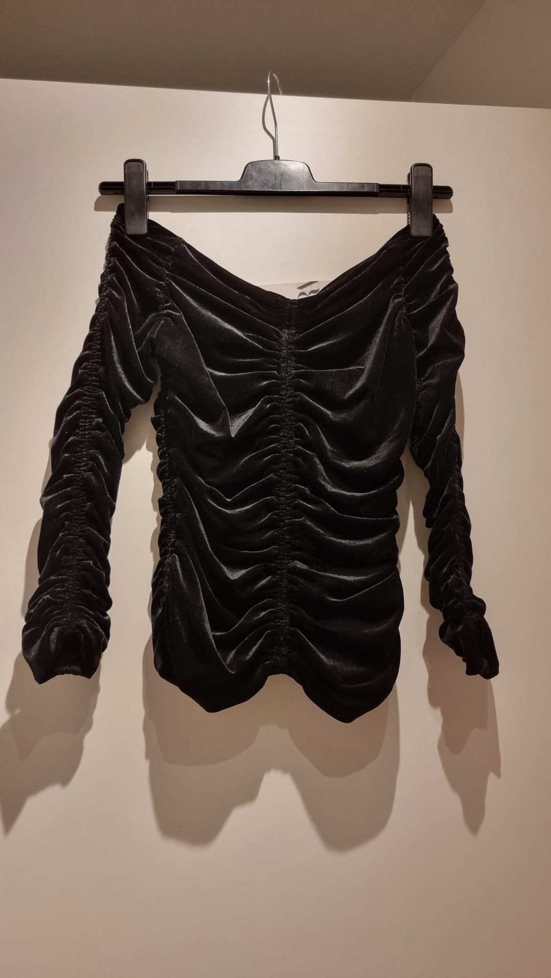Black velvet blouse with ruching, long sleeves, hanging on a black hanger against a white background.