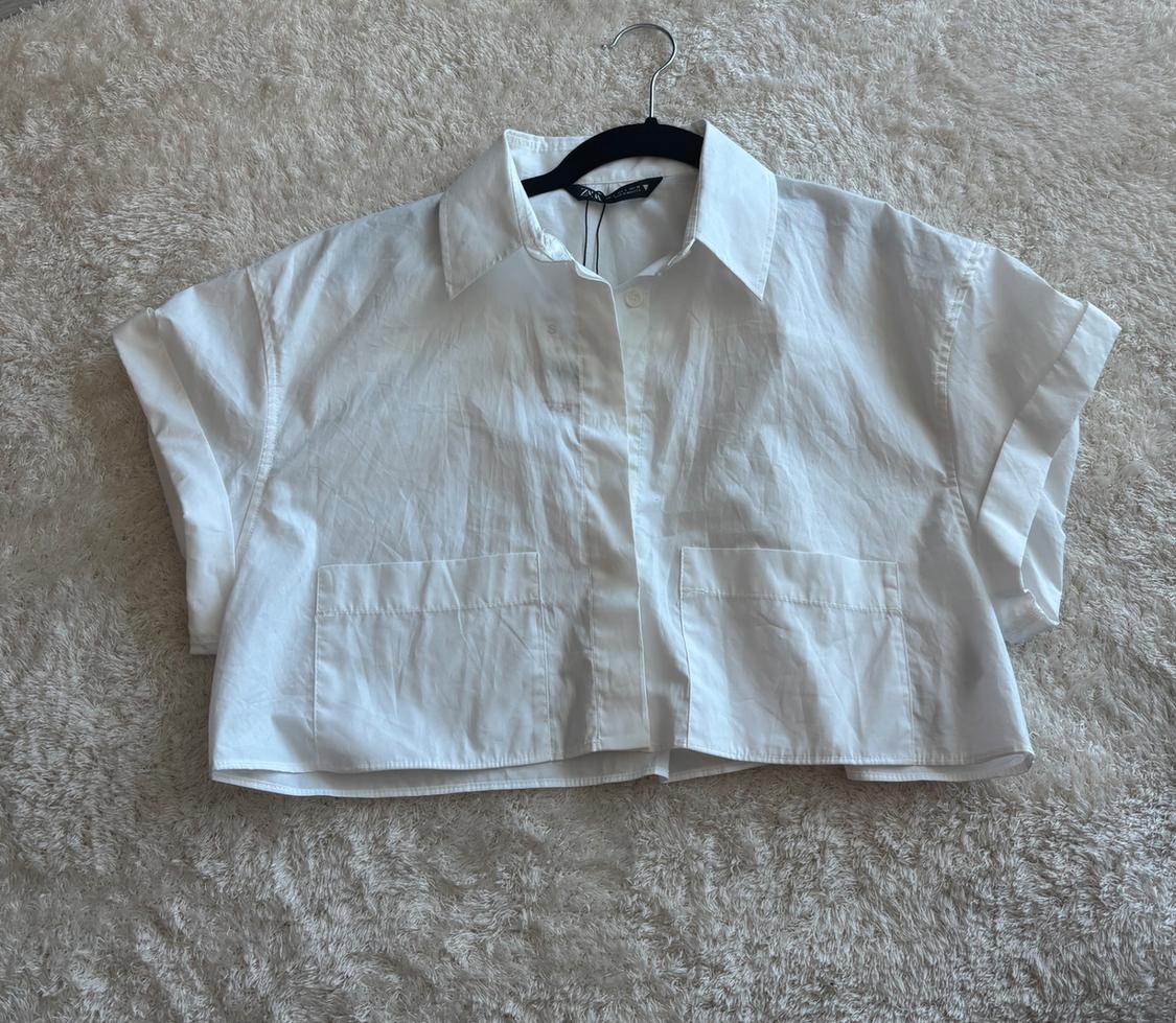 White short-sleeved shirt and classic collar, hanging on a hanger over a beige carpet.