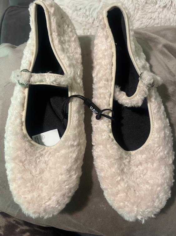 White plush shoes with buckles on a grey surface. Visible label with text "PAZ" and "ANTITECH".