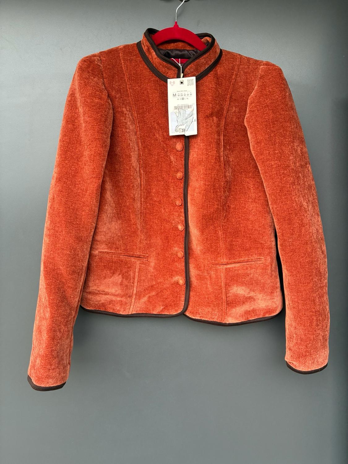Orange velvet jacket with brown piping and front buttons, hanging on a red hanger against a grey background. Label visible.