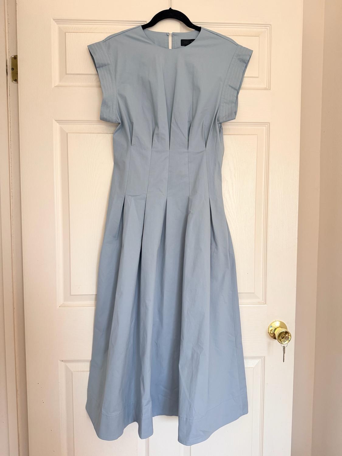 Light blue short-sleeved midi dress with pleats at the waist, hanging on a black hanger over a white door.