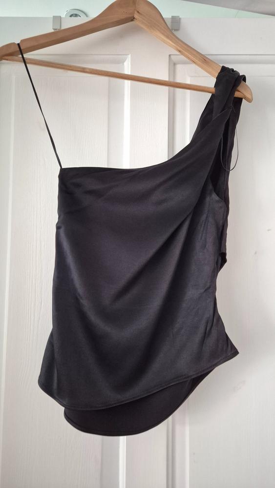 Black one-shoulder top hanging on a wooden hanger over a white door.