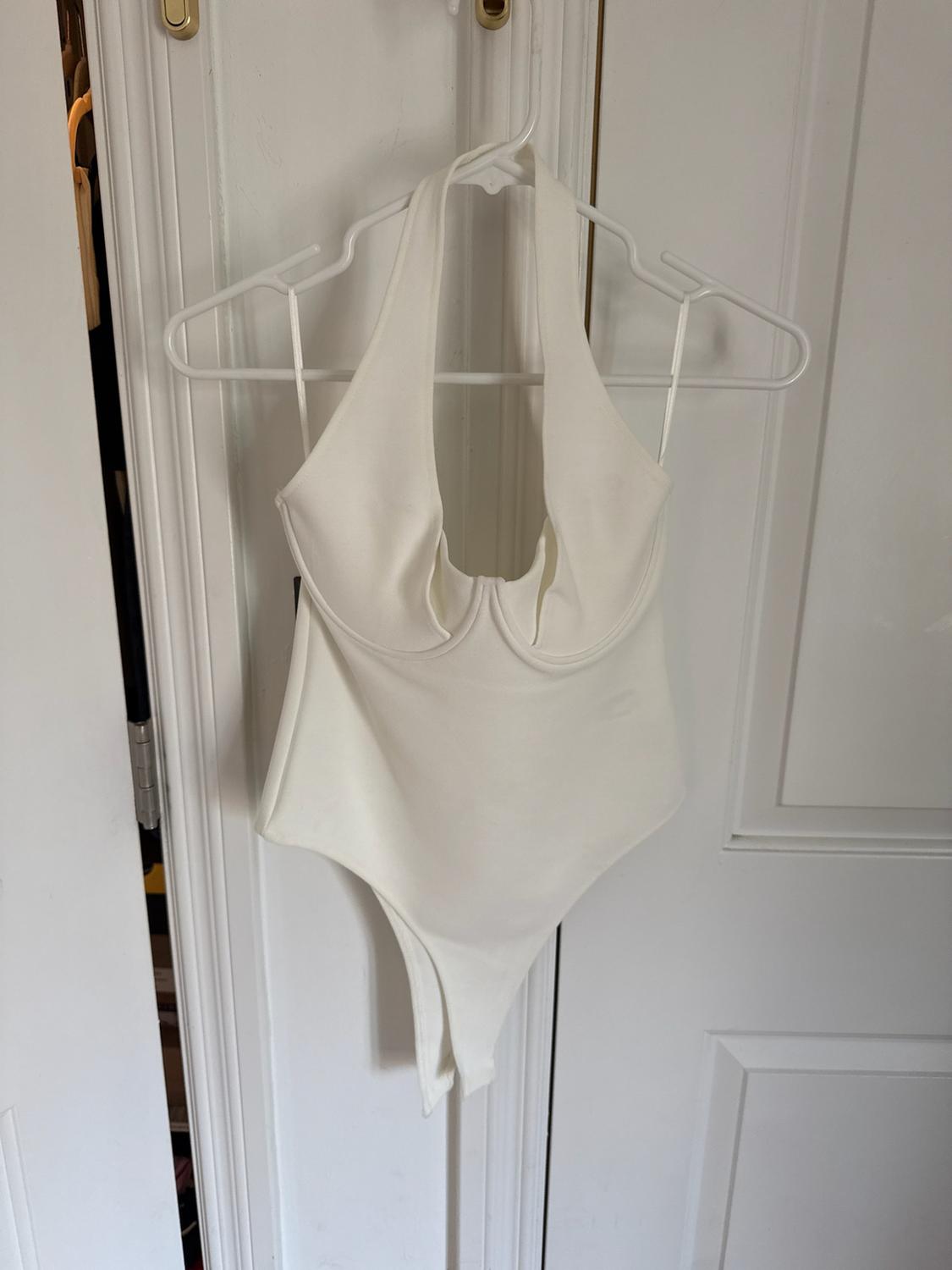 White halterneck bodysuit with ring detail, hanging on a hanger over a half-open white door.