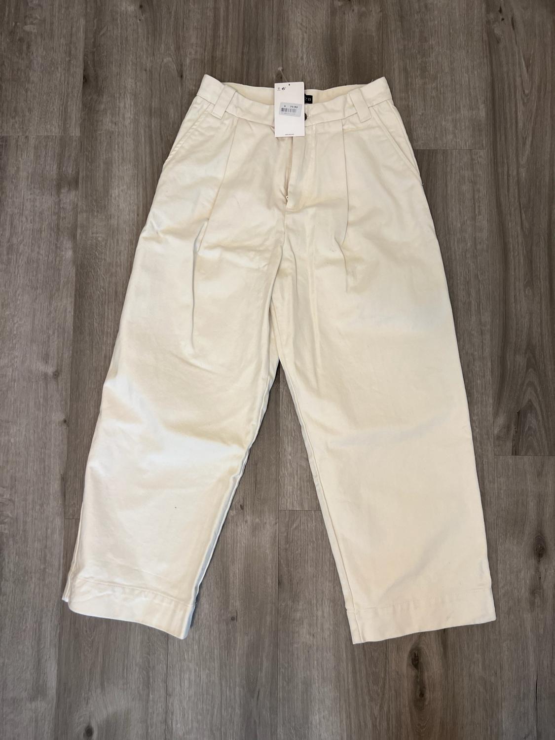 Wide-leg Ecru trousers with front pleats and belt loops, laid out on a wooden floor.