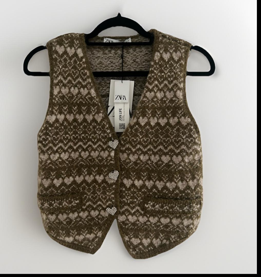 Brown knit vest with heart print and jewel buttons on a black hanger against a white background. Text: ZARA, JOIN LIFE.