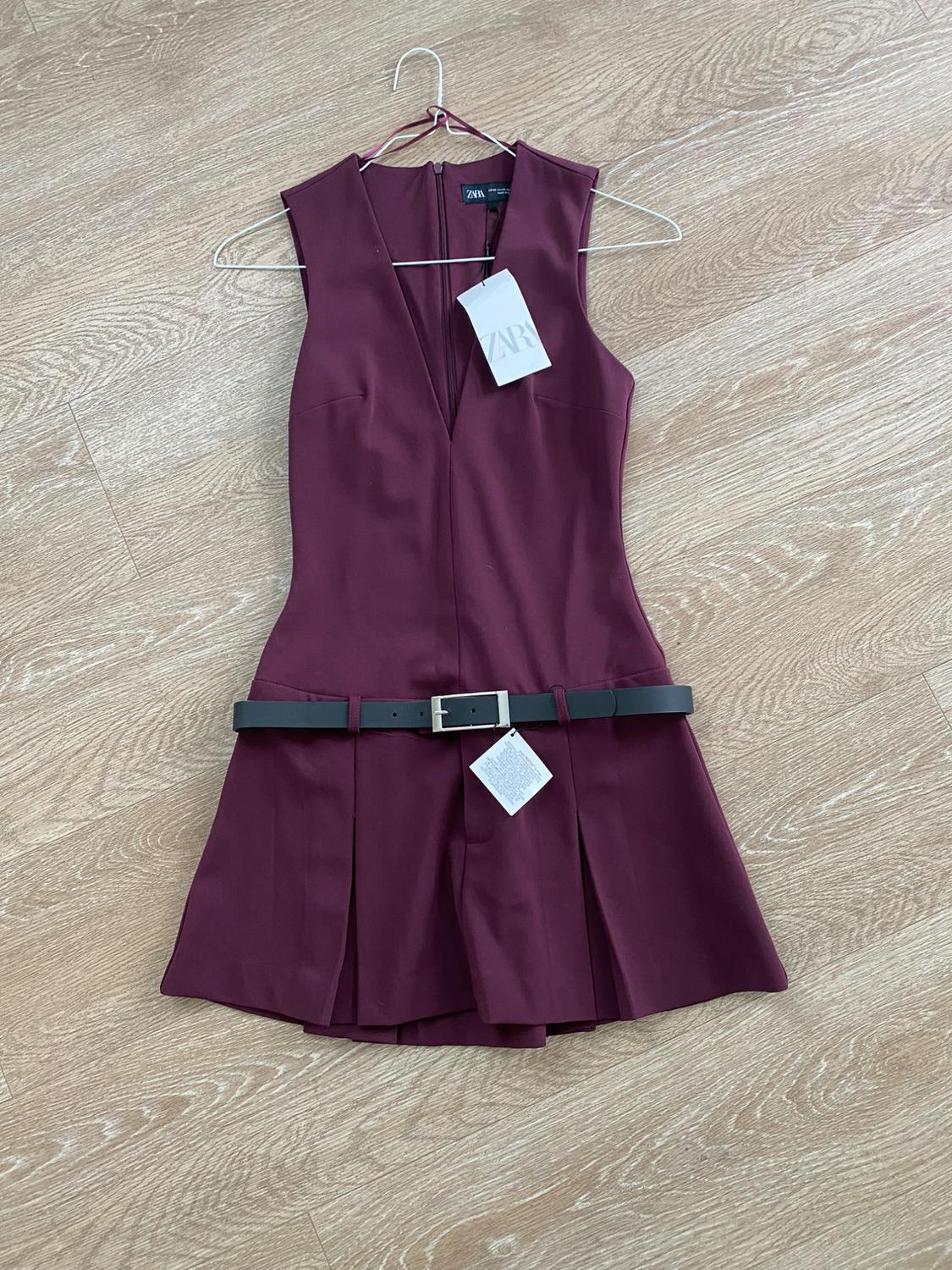 Burgundy sleeveless dress with black belt and Zara hangtag, on light wood flooring.