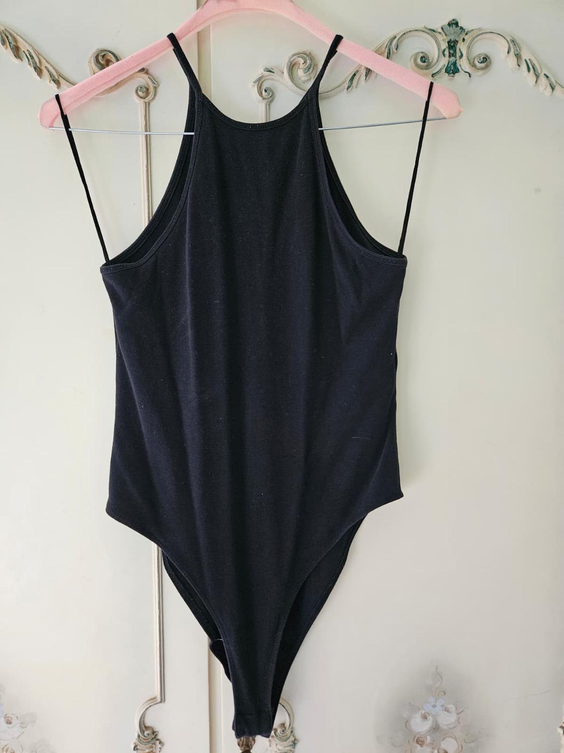 Black body with thin straps on a pink hanger, hanging in front of a vintage-style white wardrobe with carved floral details.