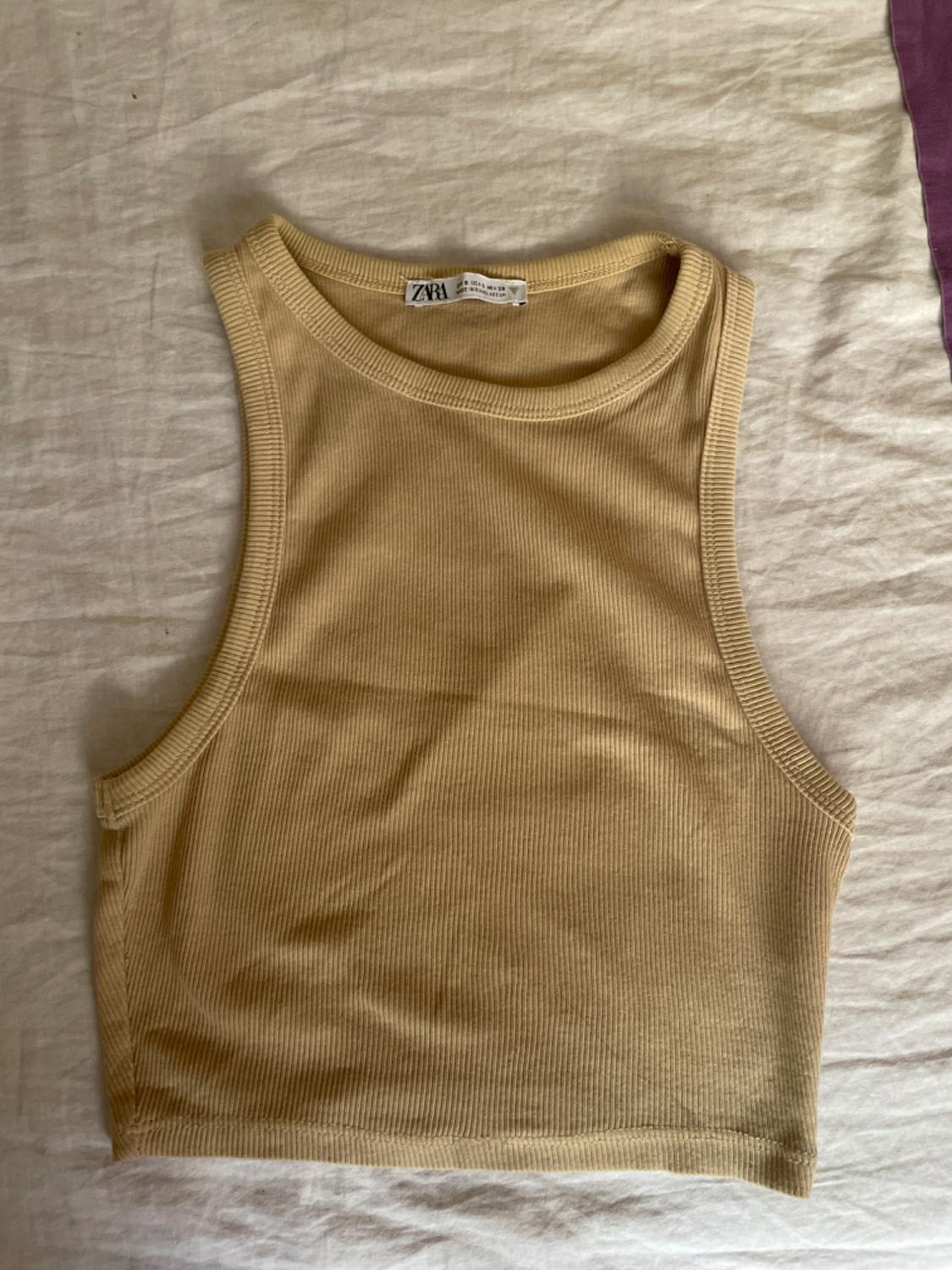 Beige sleeveless crop top on a white surface. Visible label with the text "ZARA".