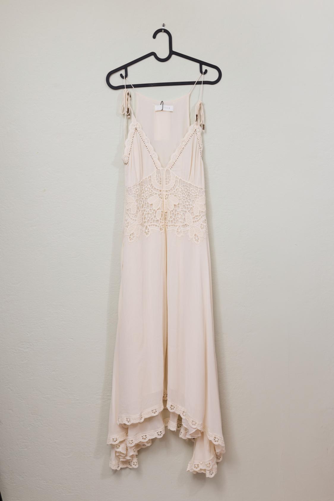 Cream-colored dress with thin straps, a detailed lace bodice, and a hem with lace trim, hanging on a black hanger.