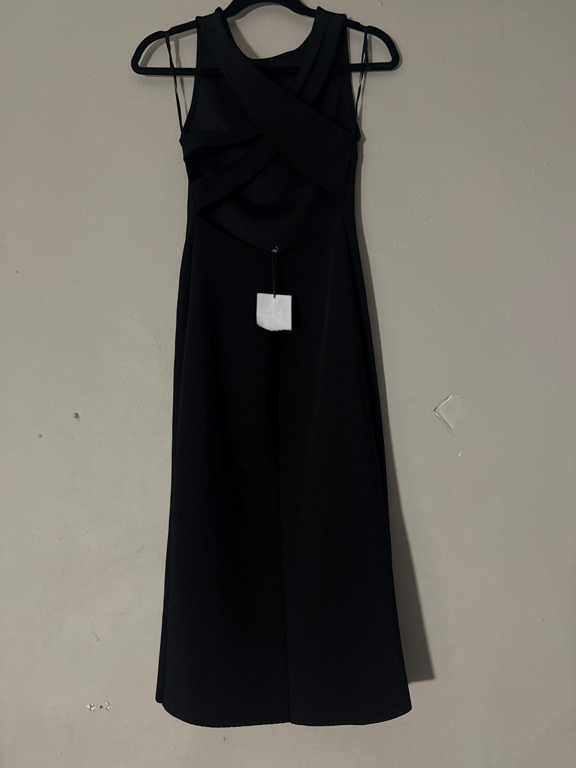Sleeveless black dress with a criss-cross design on the chest, hanging on a hanger against a beige wall. White tag visible.