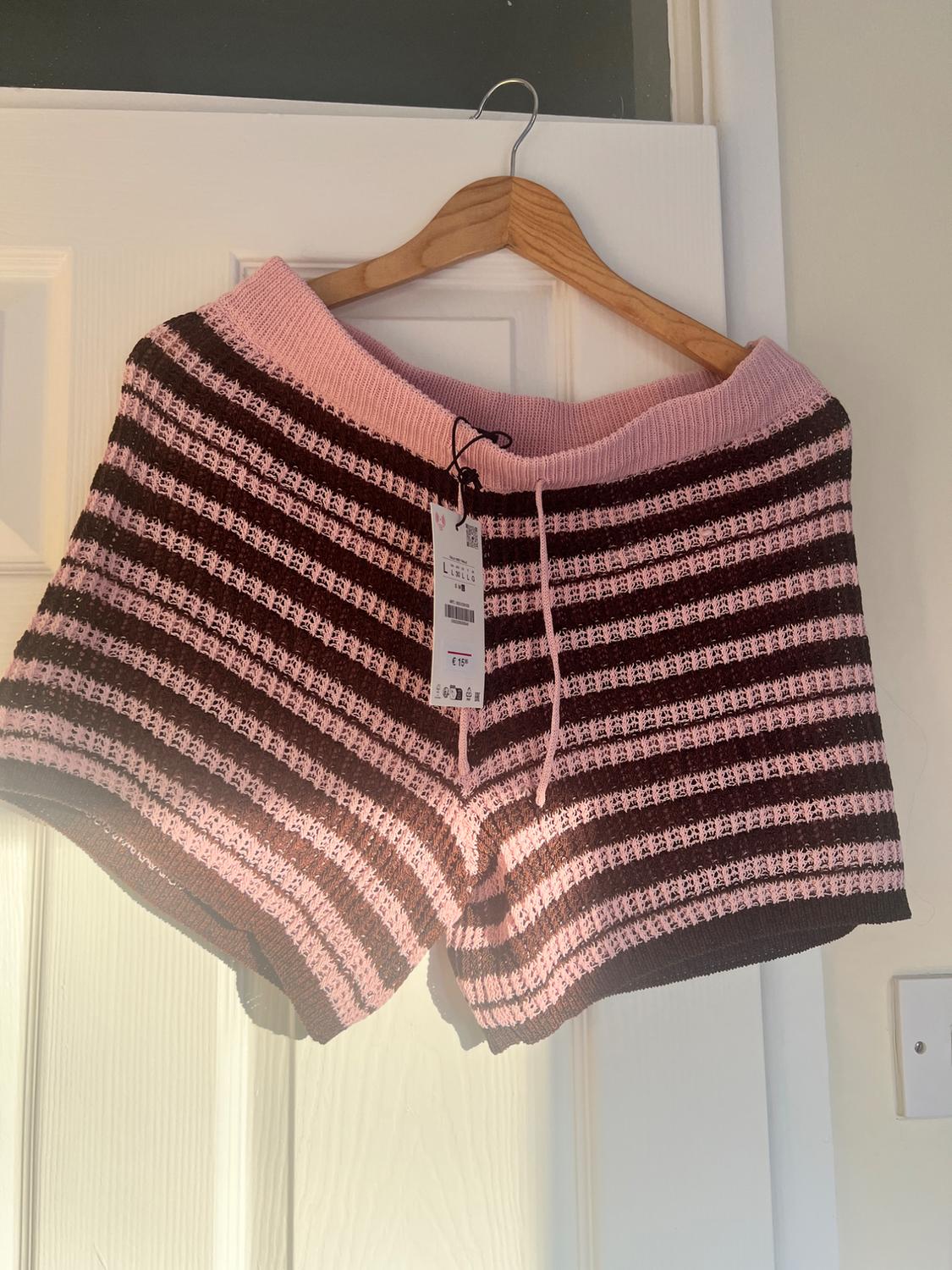 Pink and brown striped knit shorts hanging on a wooden hanger over a white door, with price tag visible.