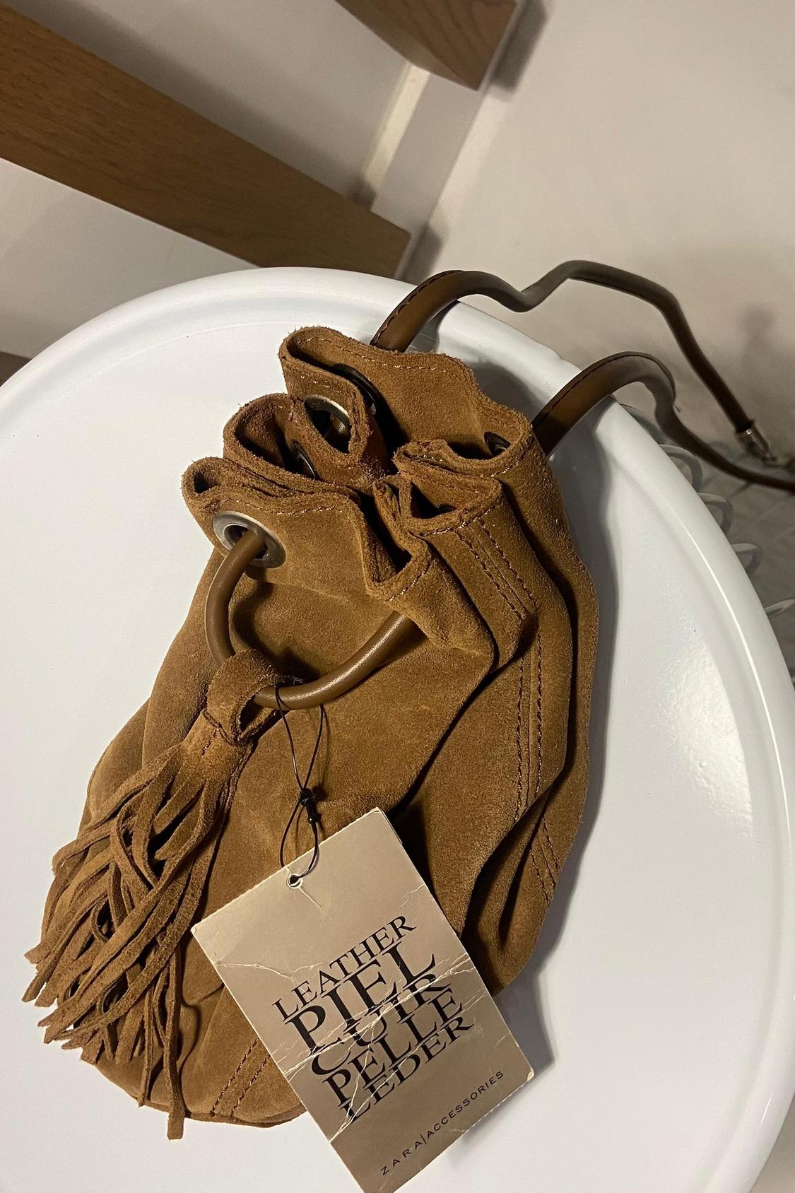 Detail of brown fringed handbag with label that says 'LEATHER PIEL CUIR PELLE LEDER'.