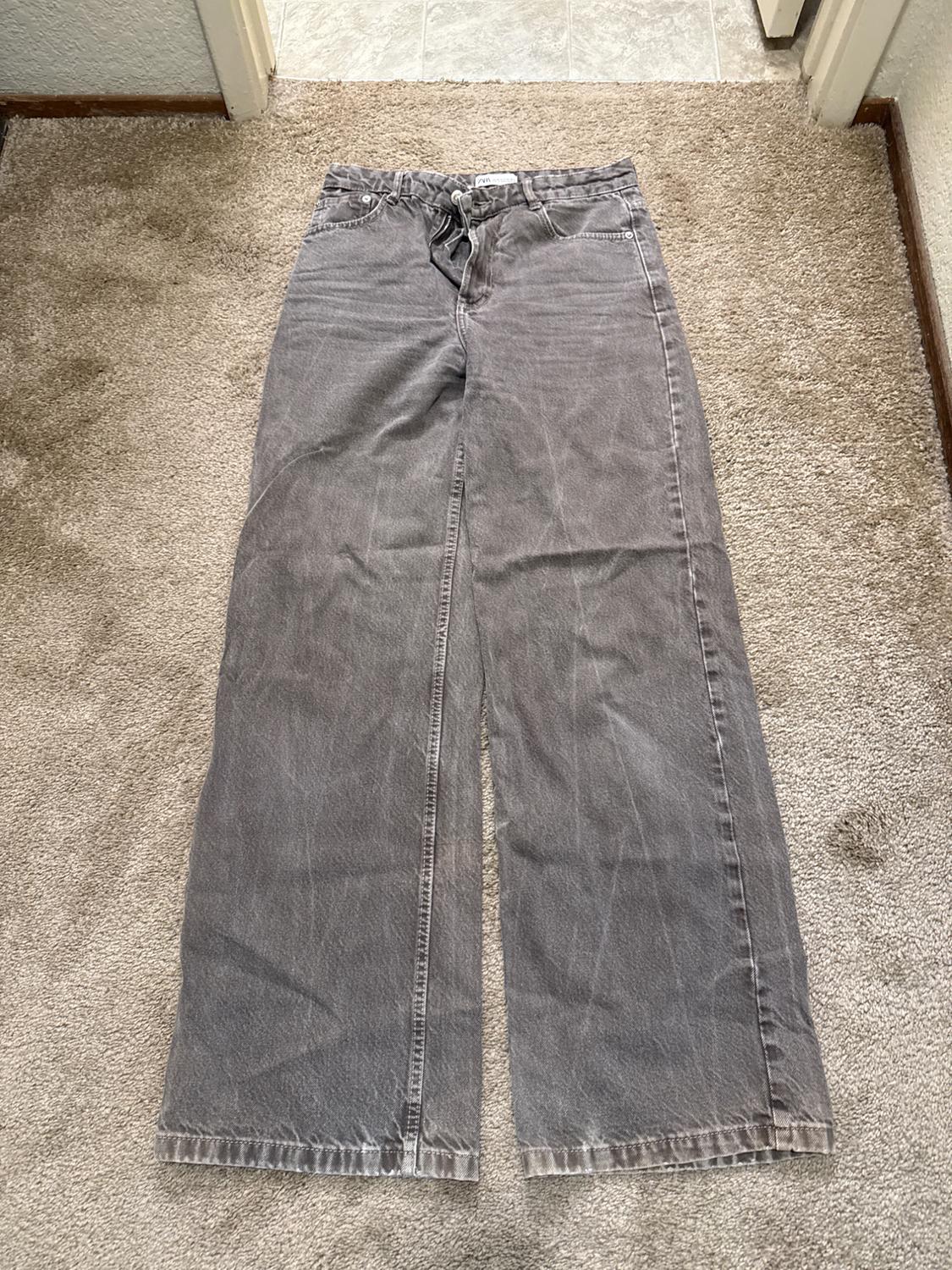 Gray wide-leg jeans with a washed effect, laid out on a beige carpet.