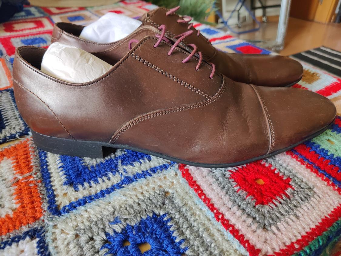 Brown dress shoes with laces on a colourful blanket.