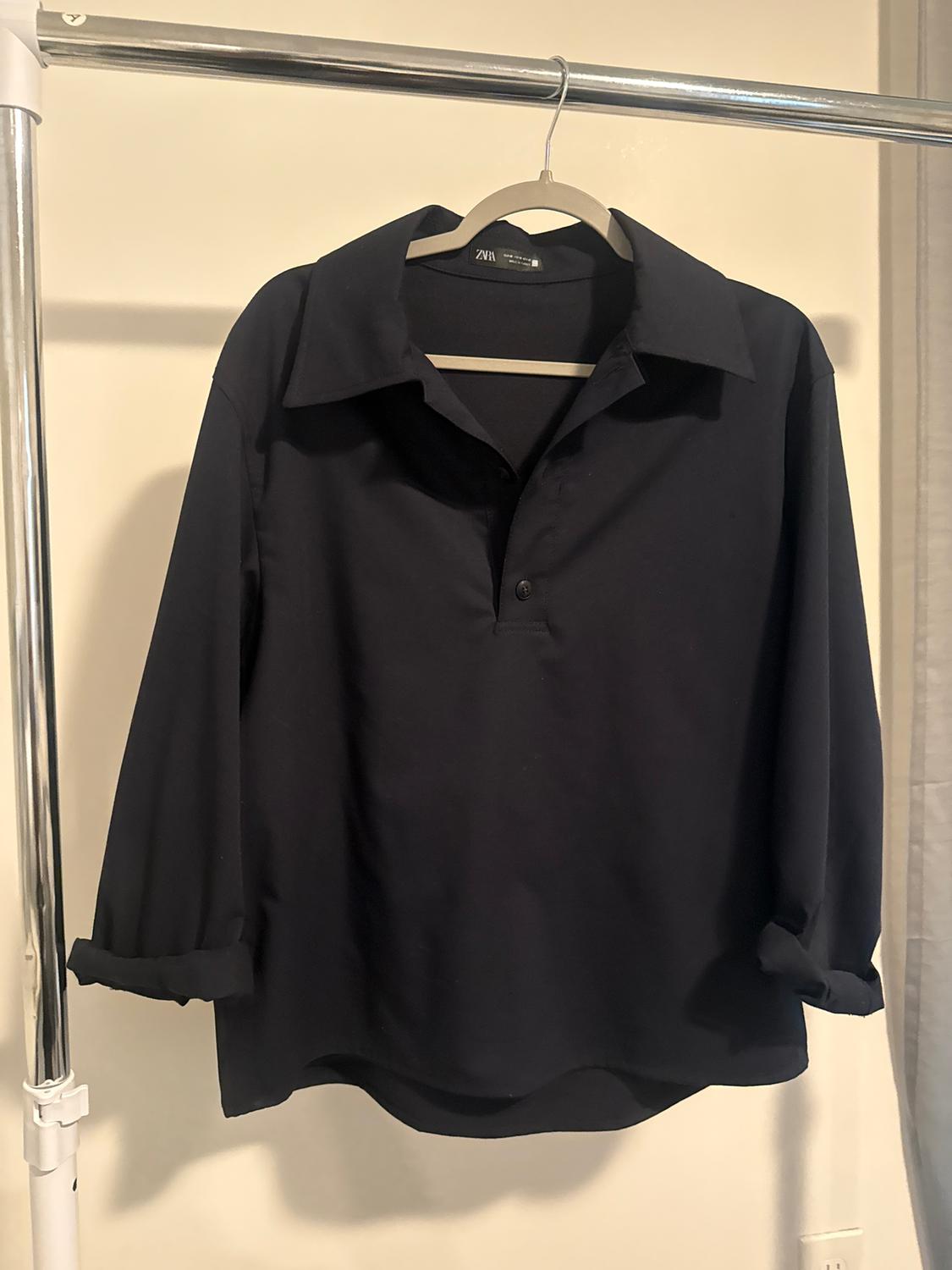 Black long-sleeved shirt hanging on a metal clothes rail. The label reads "Zara". White background and soft light.