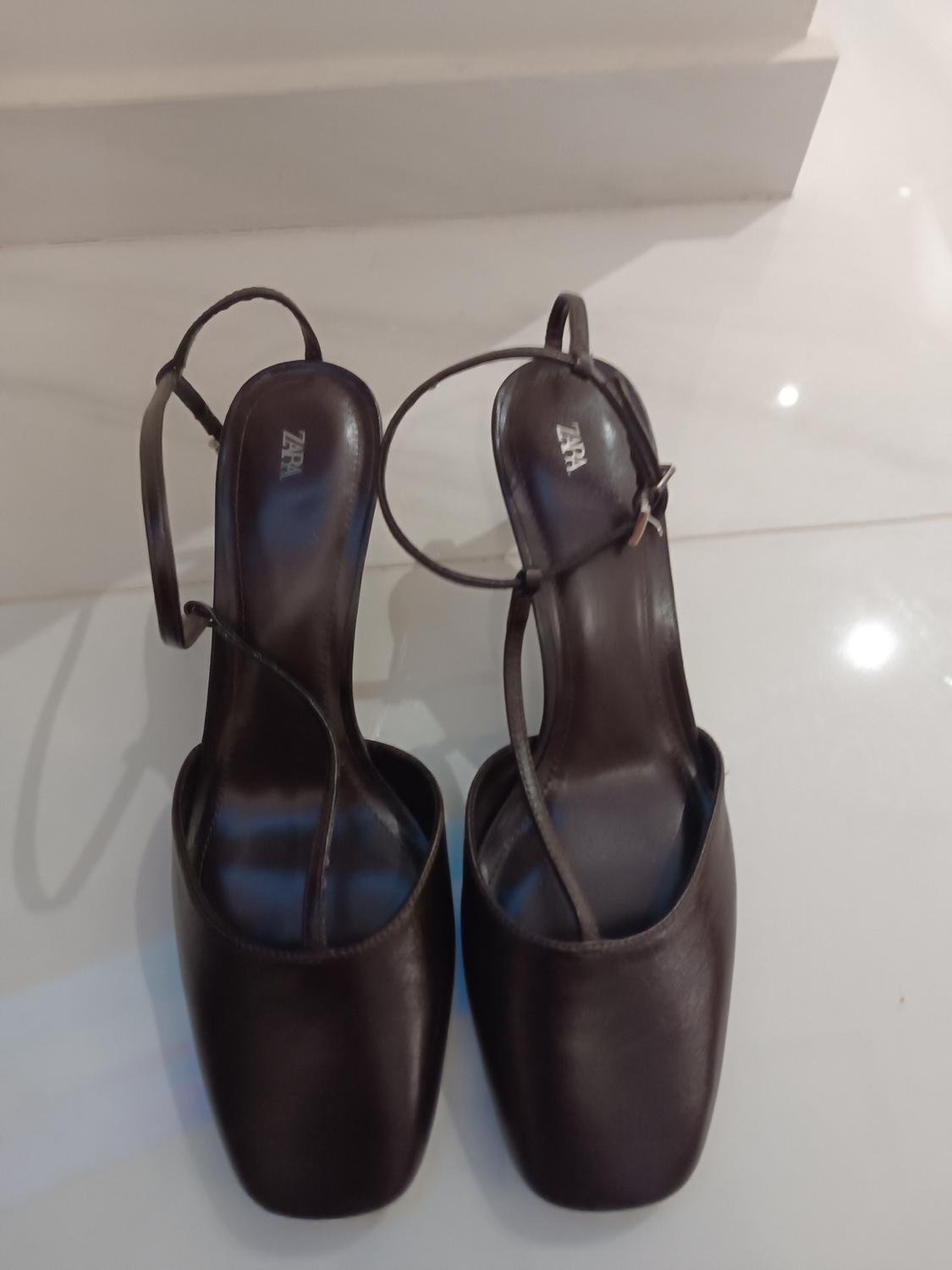 Black heeled sandals with thin straps and "ZARA" logo on the insole, on a bright white background.