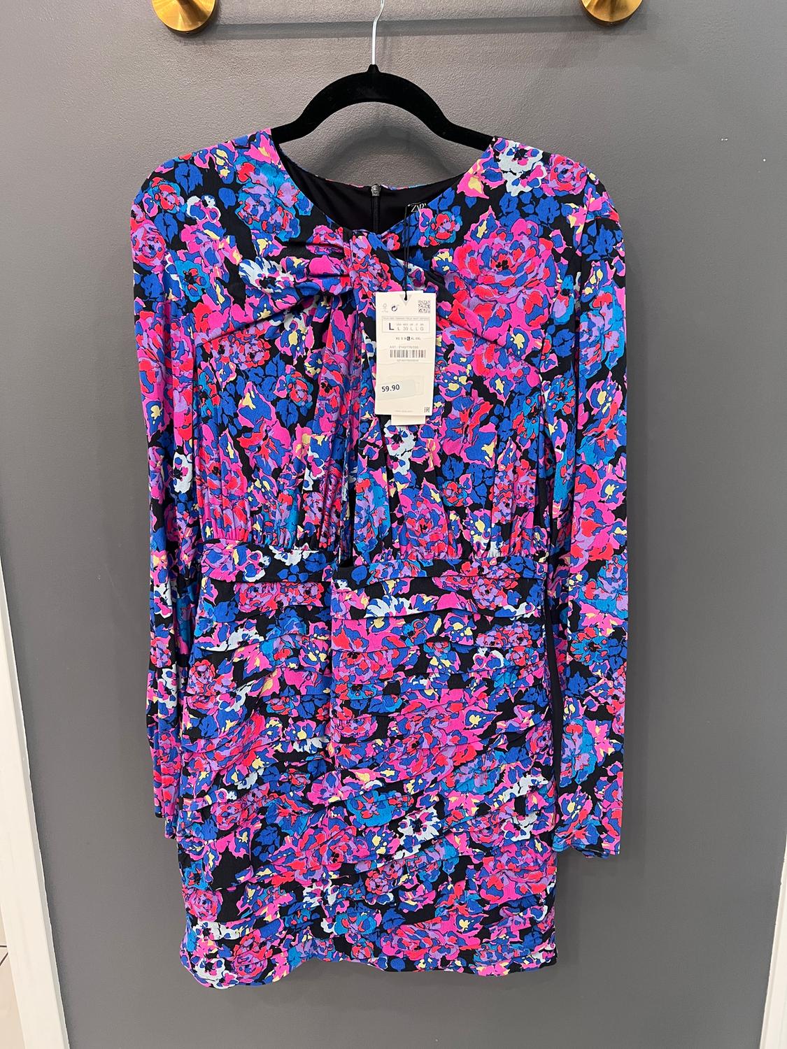 Long-sleeved dress with a floral print in shades of pink, blue, and black, hanging on a black hanger. Price tag visible.