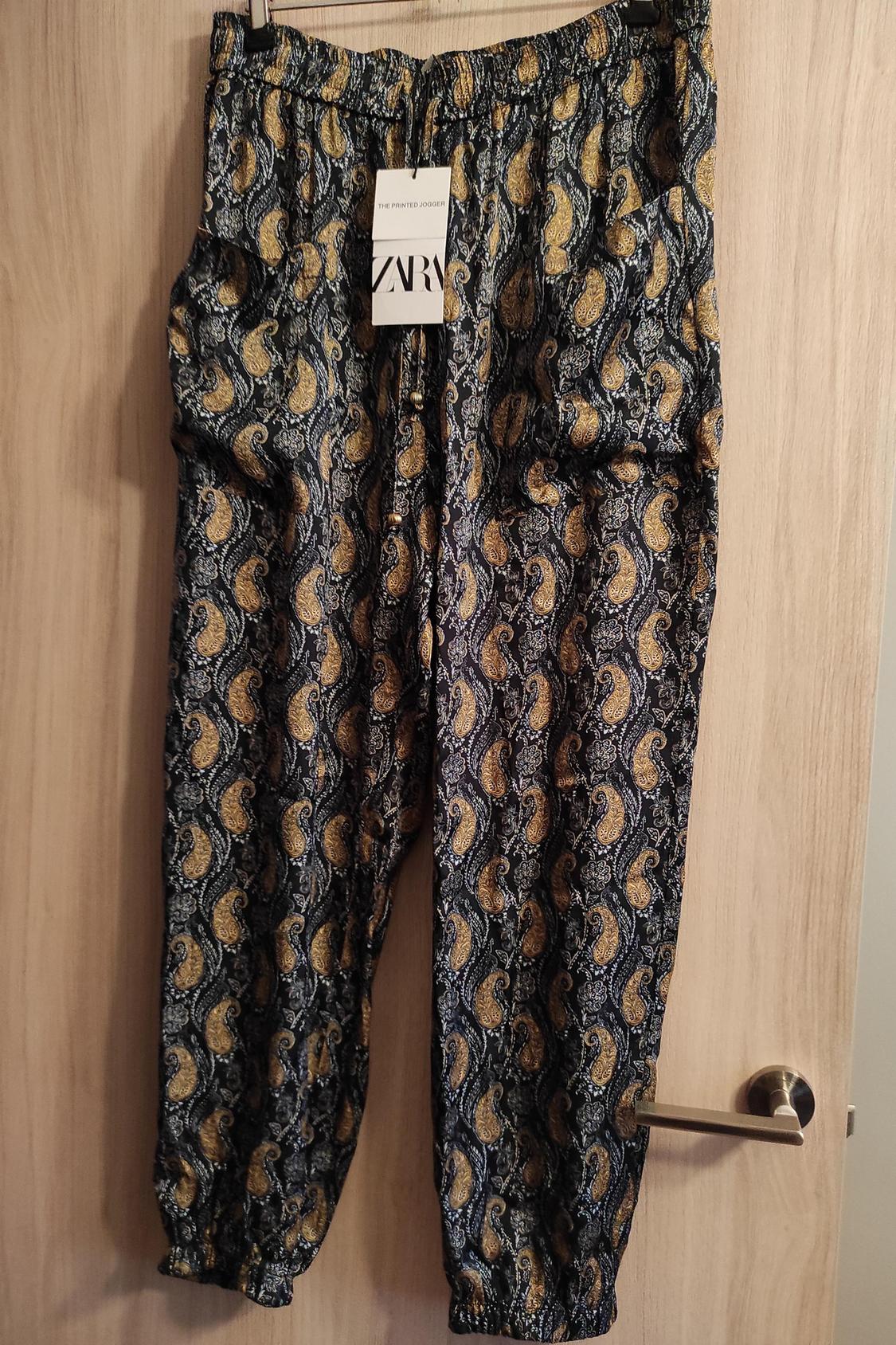 Μπροστινή όψη παντελονιού με στάμπα paisley σε αποχρώσεις του μπλε και του χρυσού, με ελαστική μέση και πλαϊνές τσέπες.