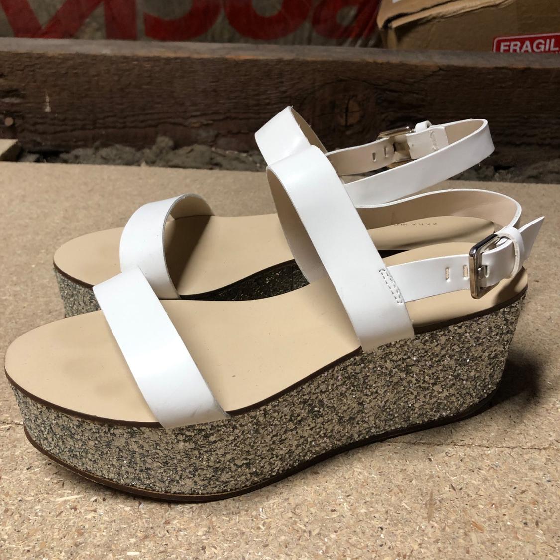 Side view of white sandals with shiny platform and metallic buckle.