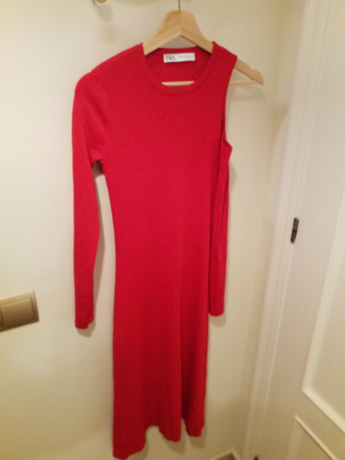 Long-sleeved red dress hanging on a wooden hanger on a white door. Label visible on the collar.