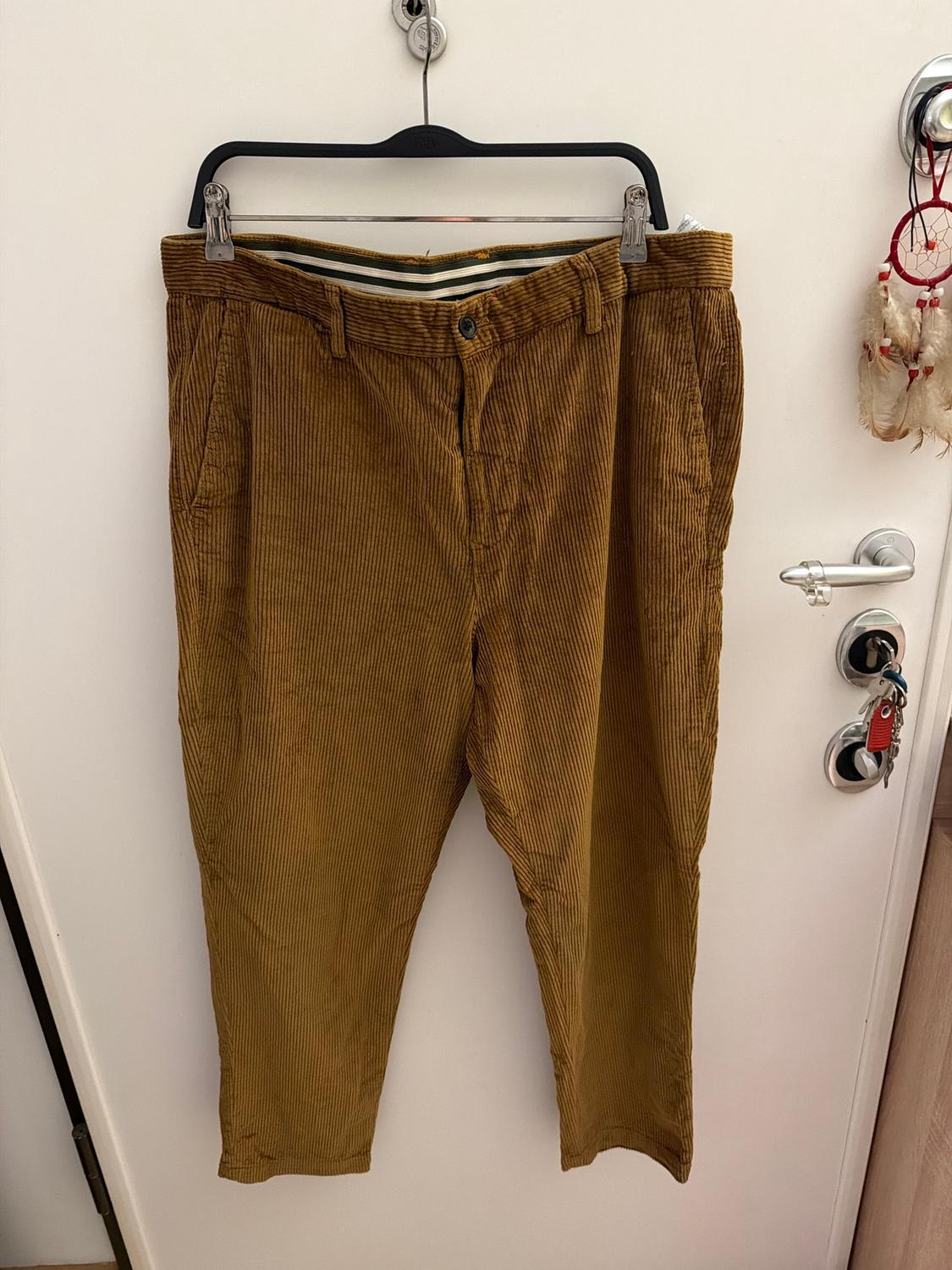 Brown corduroy trousers hanging on a black hanger over a white door, with a dreamcatcher hanging next to them.