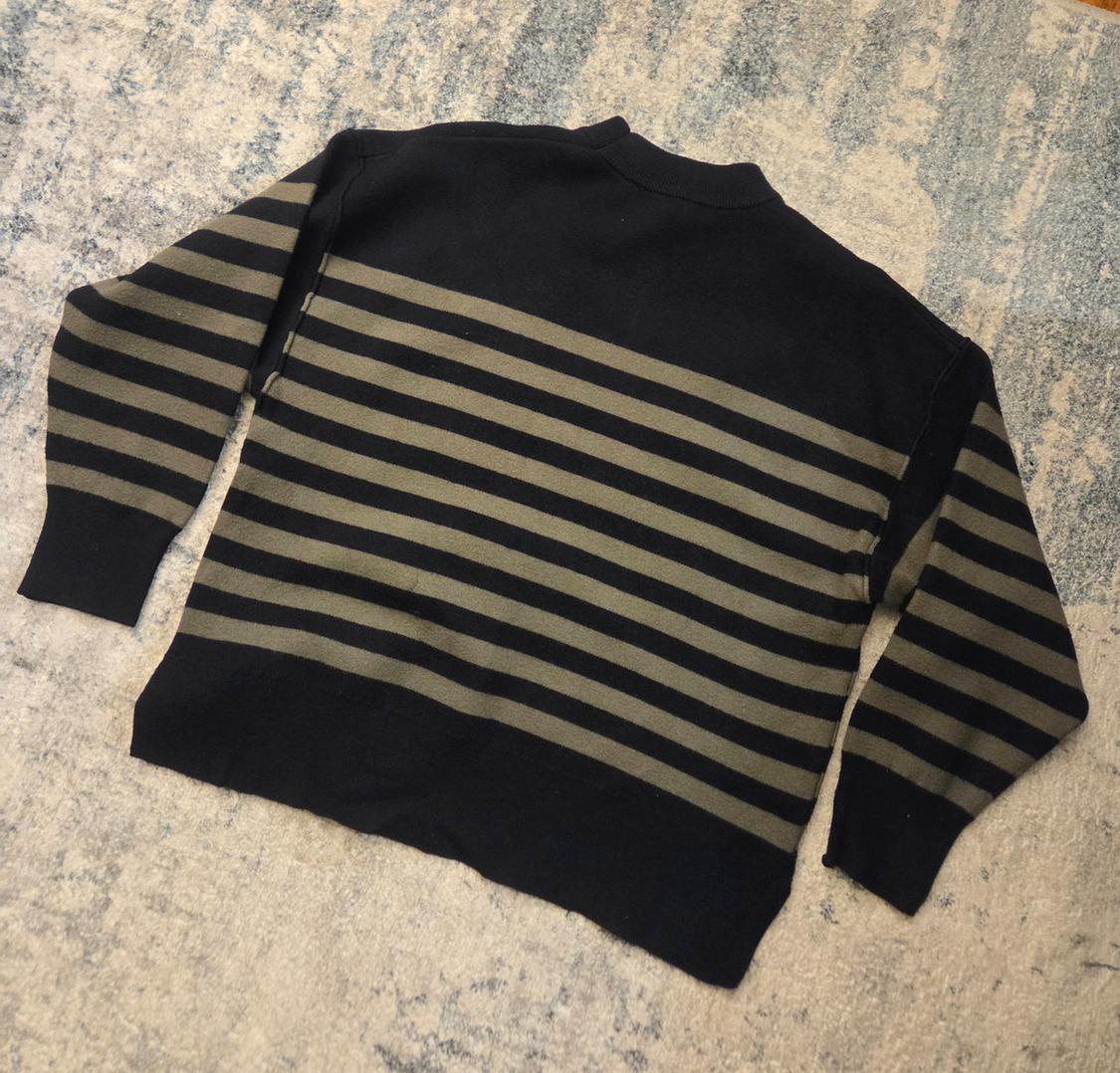 Black and grey striped jumper on a light-toned rug. Rear view, casual and relaxed design.