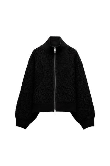 Black funnel-neck jacket with a front zip. It features a raised textured fabric, with ribbed cuffs and hem against a white background.
