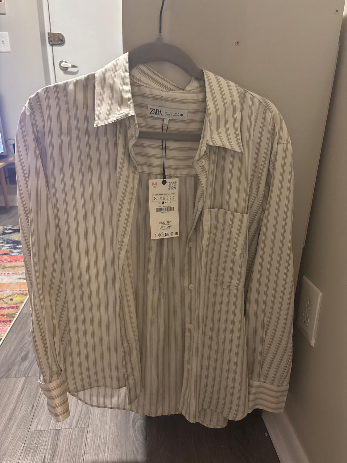 Light-coloured vertical striped shirt hanging on a hanger. Visible tag with price: US$ 49.90, UK: 29.99.