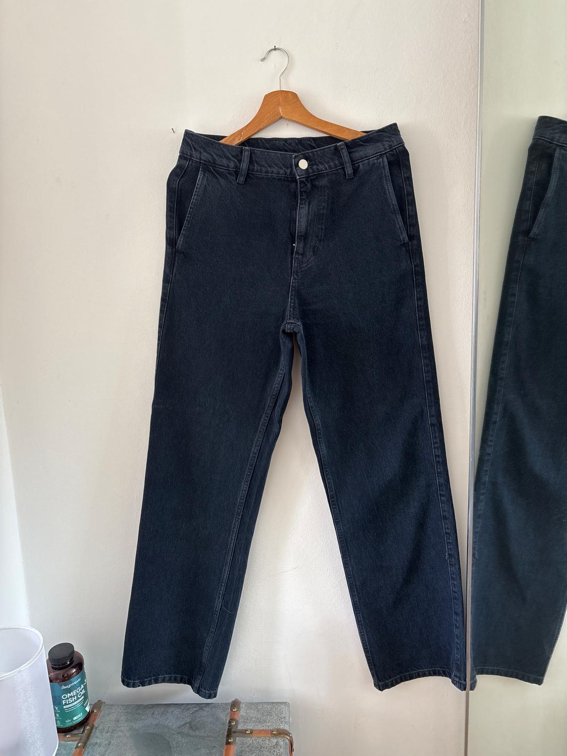 Dark denim jeans on a wooden hanger against a white wall next to a mirror. Below is a trunk and a jar with the text OMEGA-3 FISH OIL.