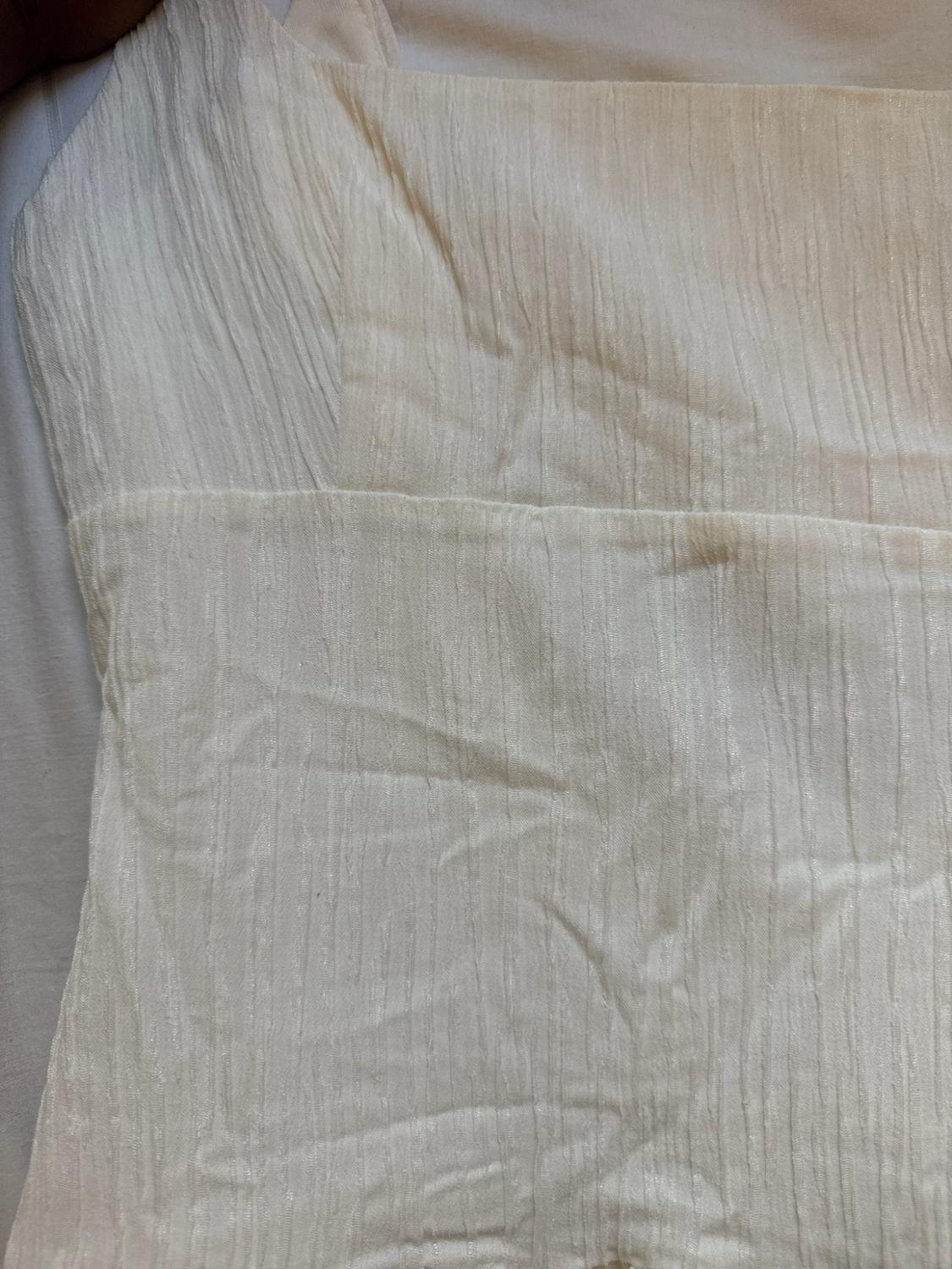 Close-up of the fabric of an ecru garment with a crinkled texture and a horizontal seam.