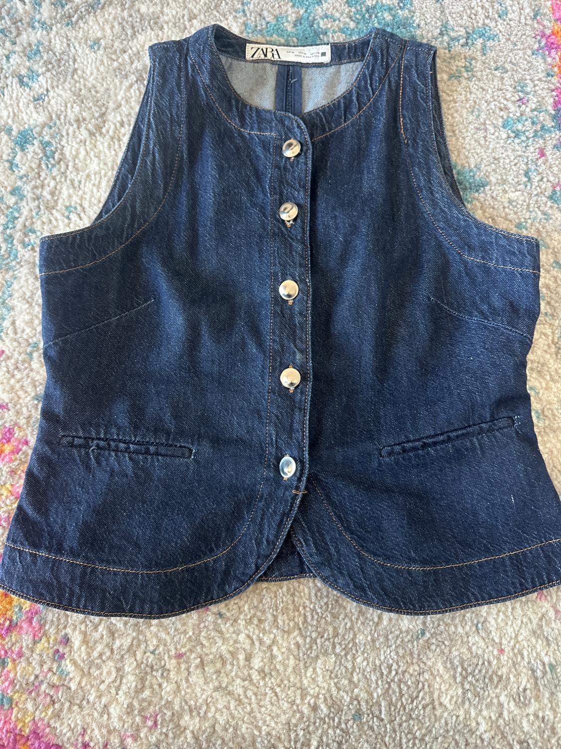 Blue denim waistcoat with front buttons on a colourful rug. Visible tag with text "ZARA".