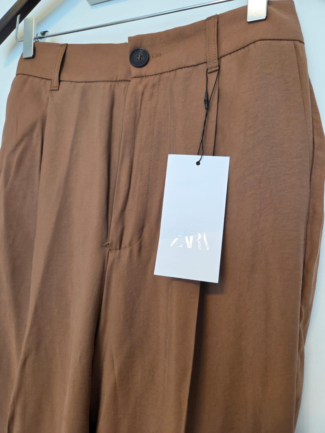 Detail of brown trousers with black button and visible label.