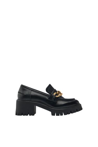 Side view of a black shoe with a chunky heel and gold chain detail on the vamp.