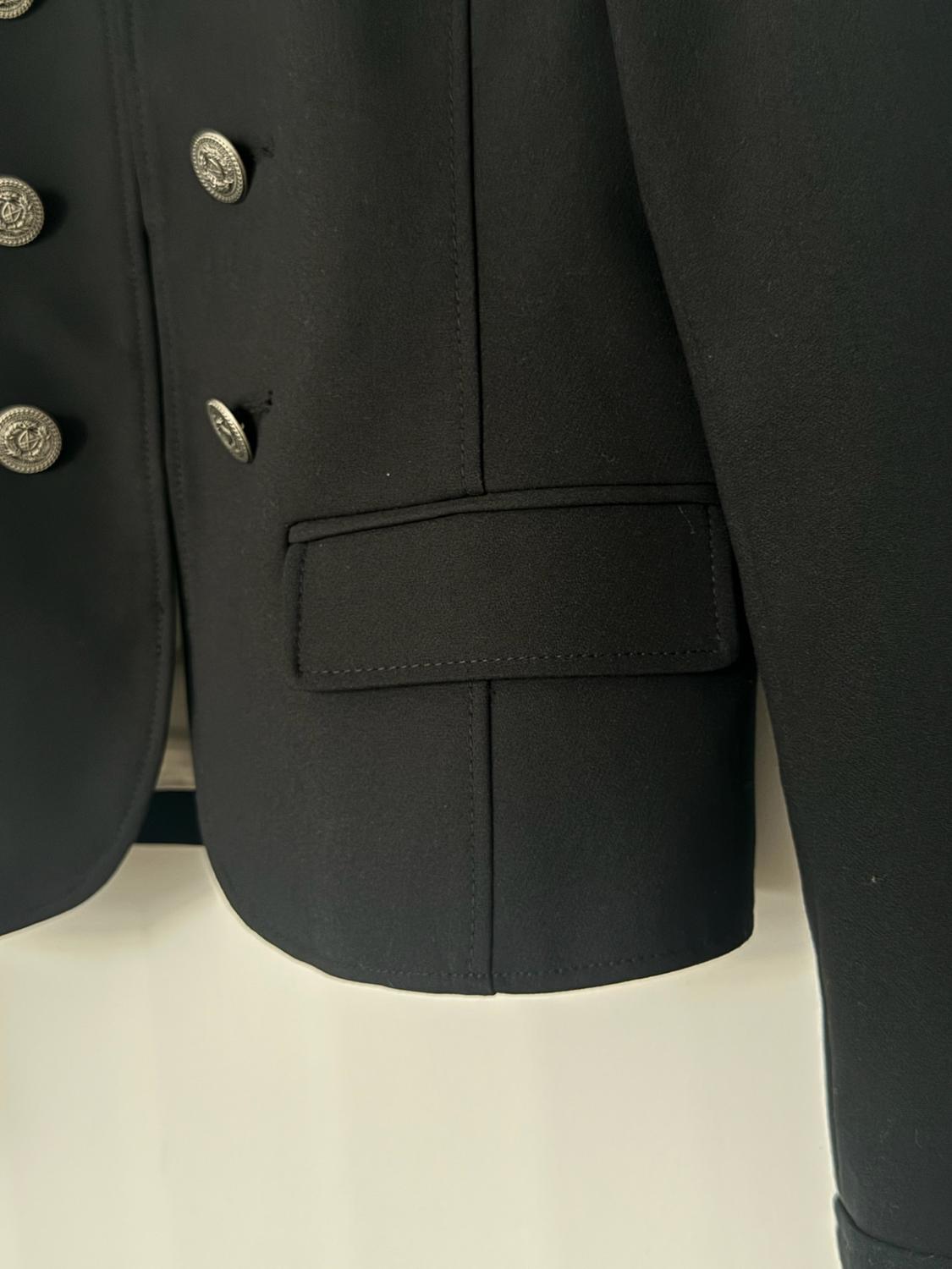 Close-up of a black blazer with embossed silver buttons and a flap pocket on a white background.