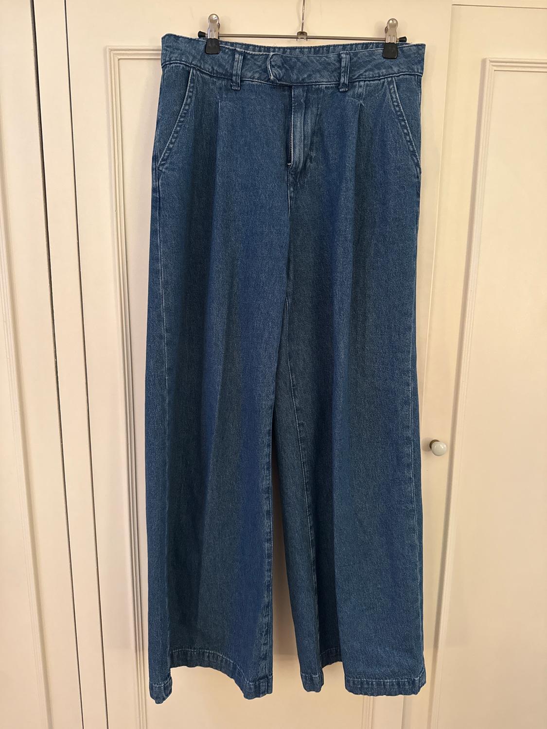 Wide-leg jeans hanging on a hanger over a white door. Blue denim fabric with pockets and belt loops.