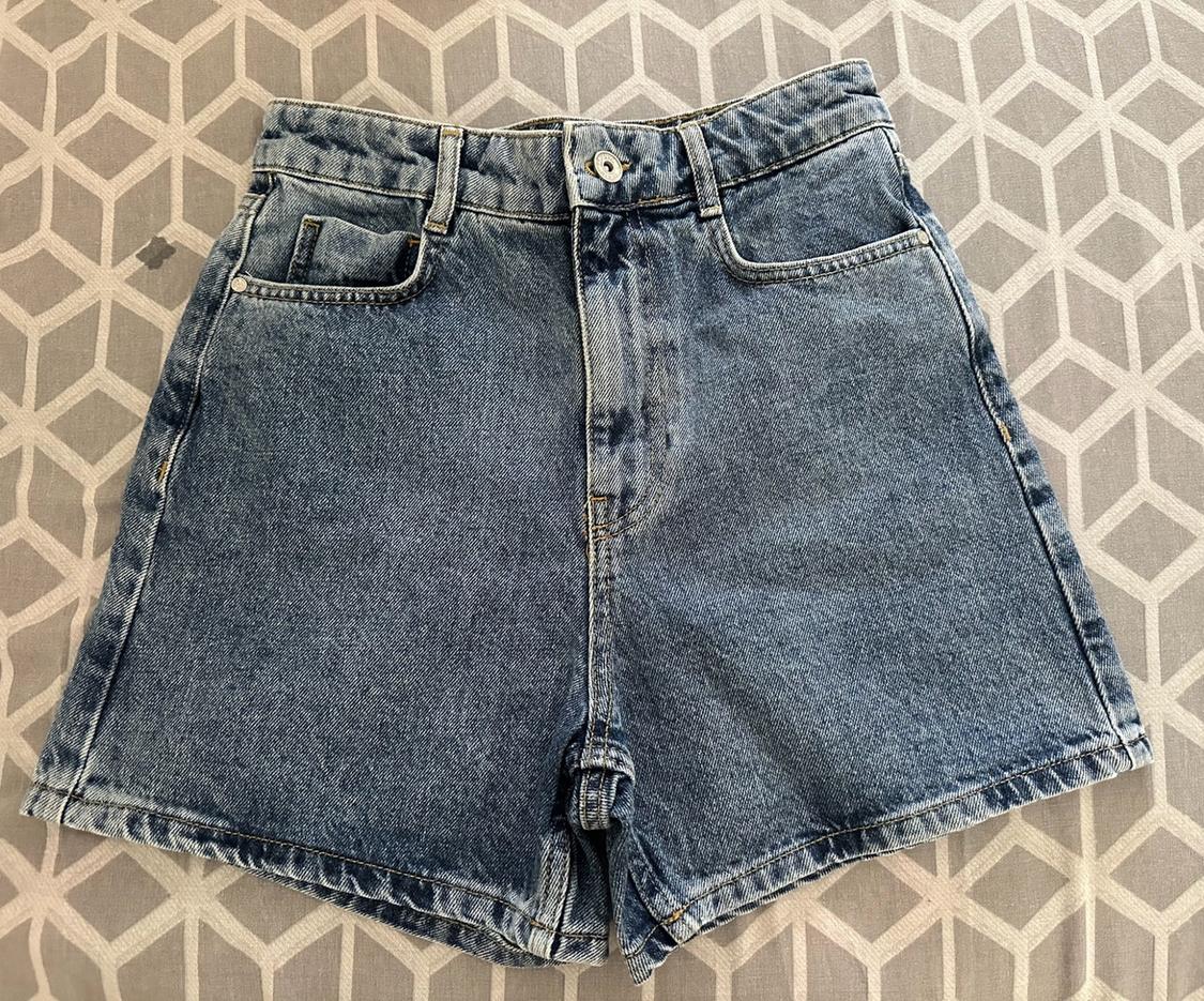 Blue denim shorts on a grey geometric-patterned surface. Casual design with pockets and a button.