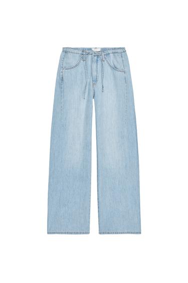 Front view of wide-leg, light blue denim trousers with side pockets and adjustable waistband.