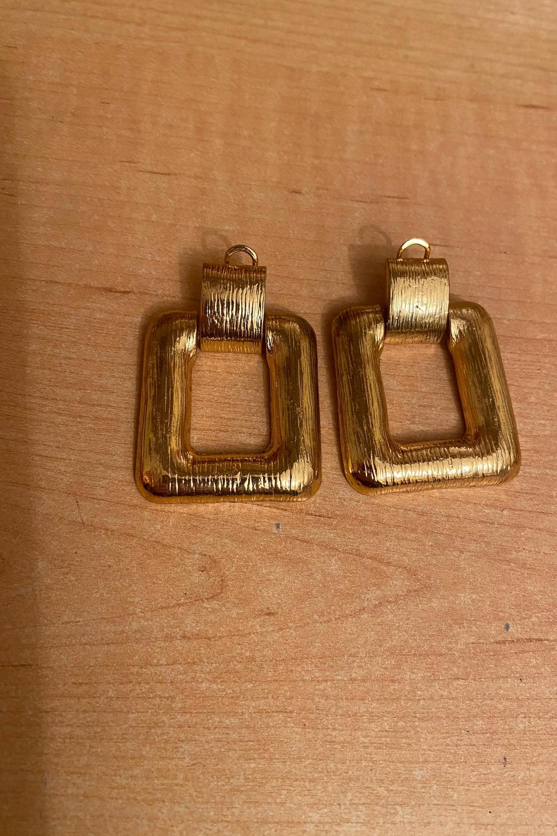 Pair of square gold textured earrings on a wooden surface.
