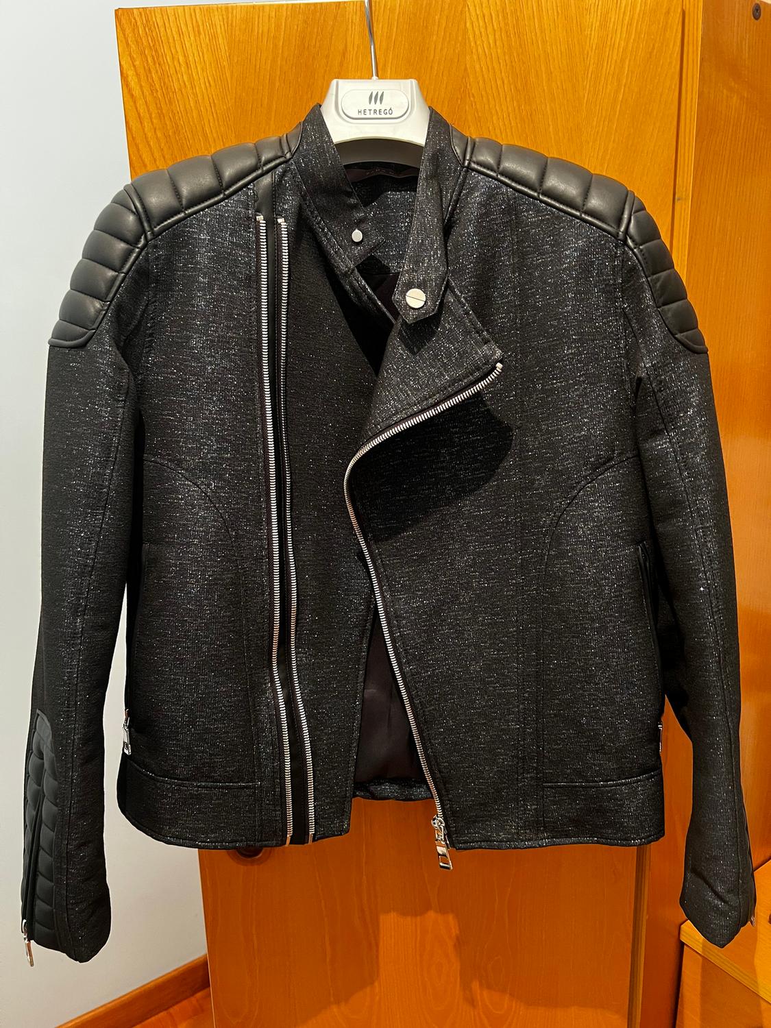 Black jacket with silver zips and quilted details on the shoulders and sleeves, hanging on a Hetrego hanger.