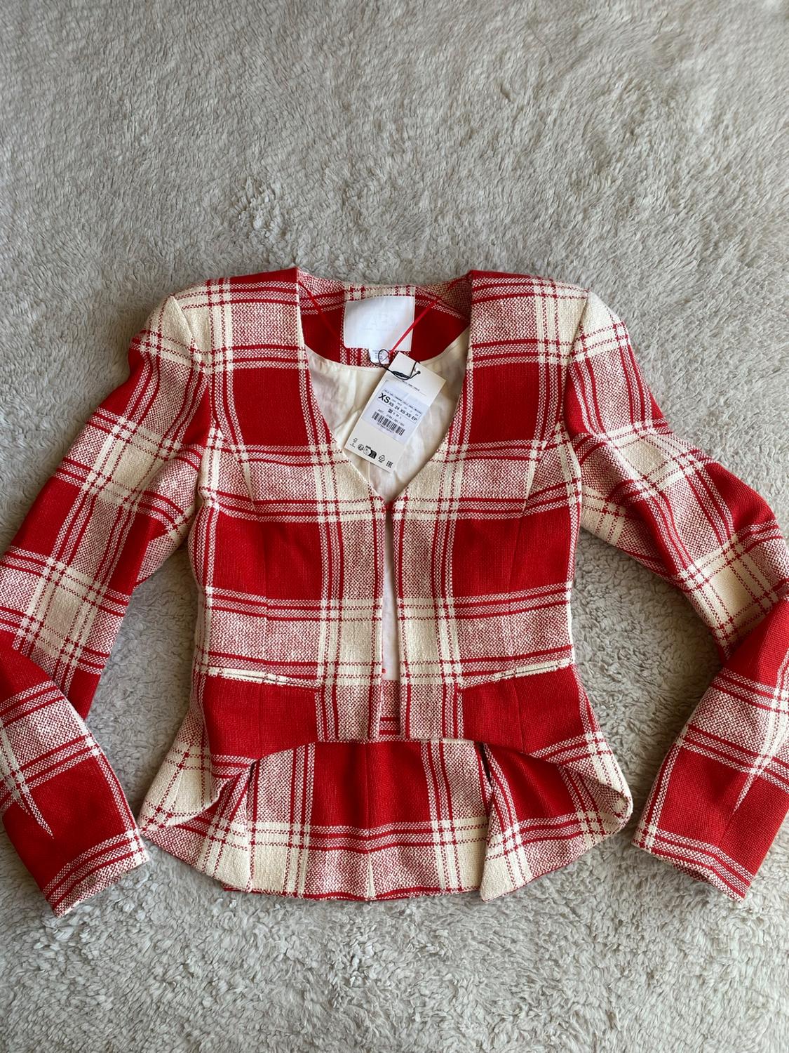 Red and white checked jacket, long sleeves and flared hem, on a shaggy rug. Visible label with text XS.