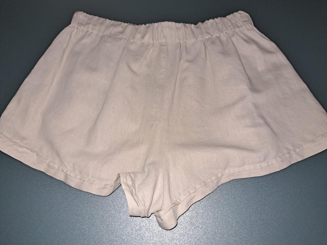 Light beige shorts with an elasticated waist and a loose fit, on a smooth, dark grey surface.