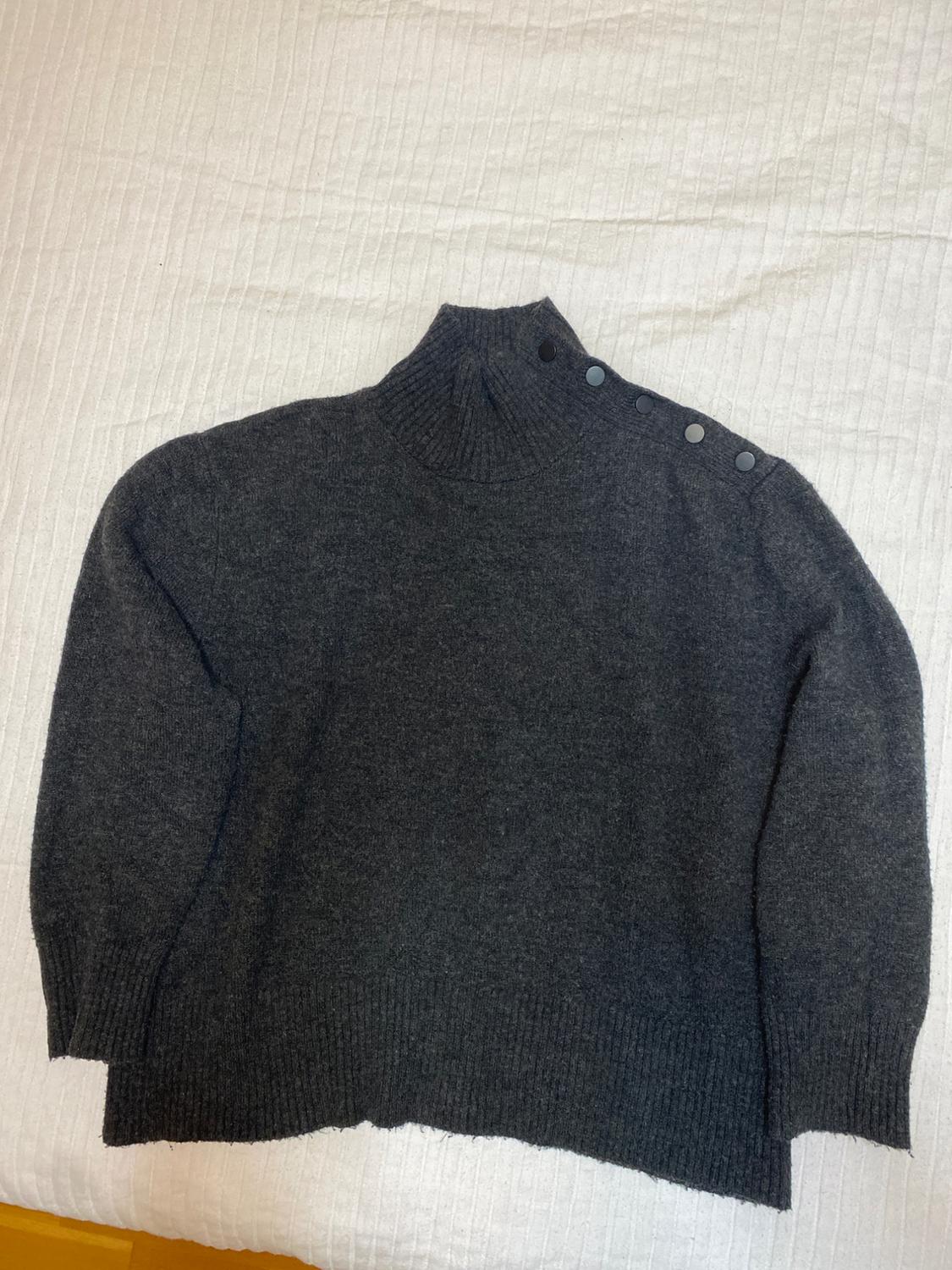 Dark grey roll-neck jumper with shoulder buttons, on a textured white surface.