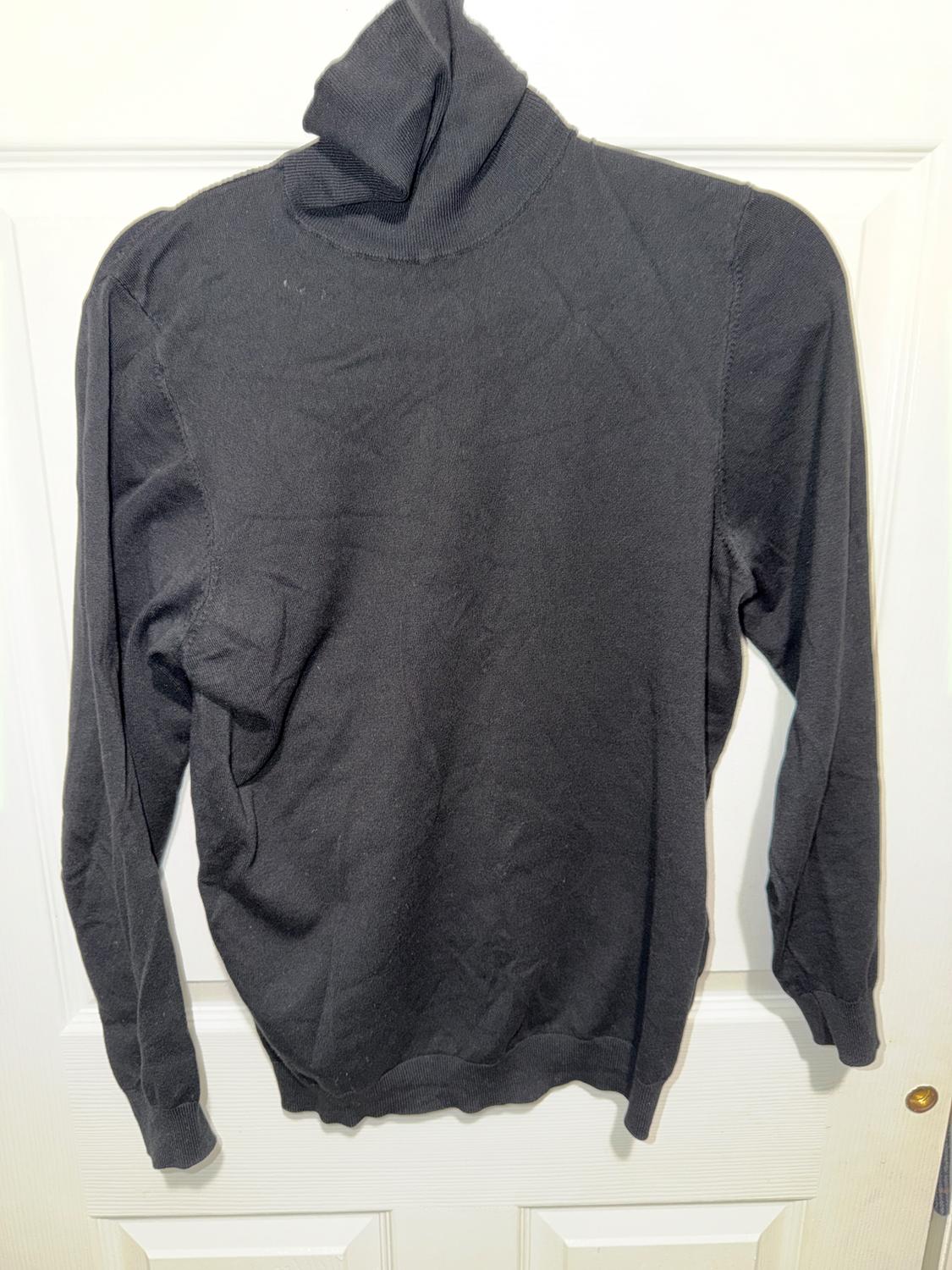 Black polo neck jumper hanging on a white door, showing a simple and classic design with long sleeves.