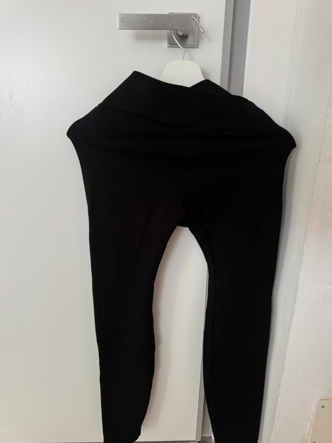 Black trousers hanging on a white hanger over a white door. The image displays a minimalist and simple style.