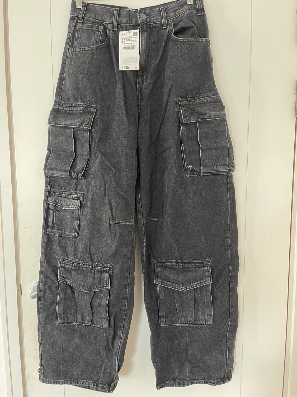 Dark grey cargo jeans with multiple flap pockets, hanging in front of a white door.