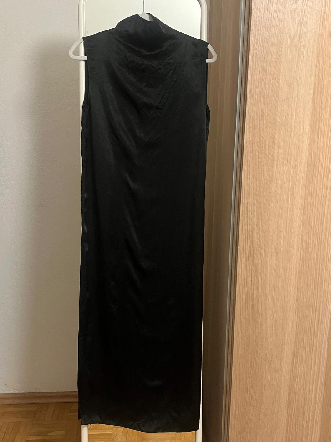 Long, black, sleeveless dress hanging on a white clothes rail, located in a room with a wooden floor and white wall.